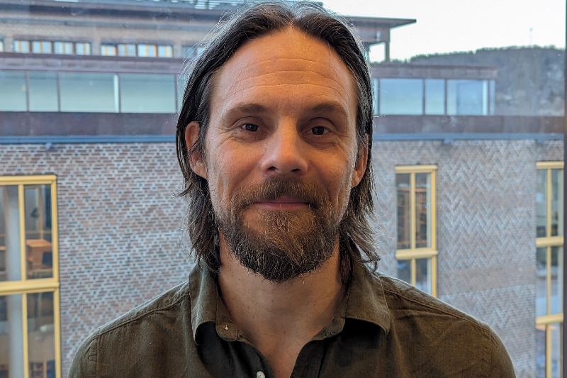 jonas jakobsen foto kjetil rydland.jpg Ein mann med skjegg og halvlangt hår poserar foran eit vindauge. Ein brun mursteinsbygning i bakgrunnen.